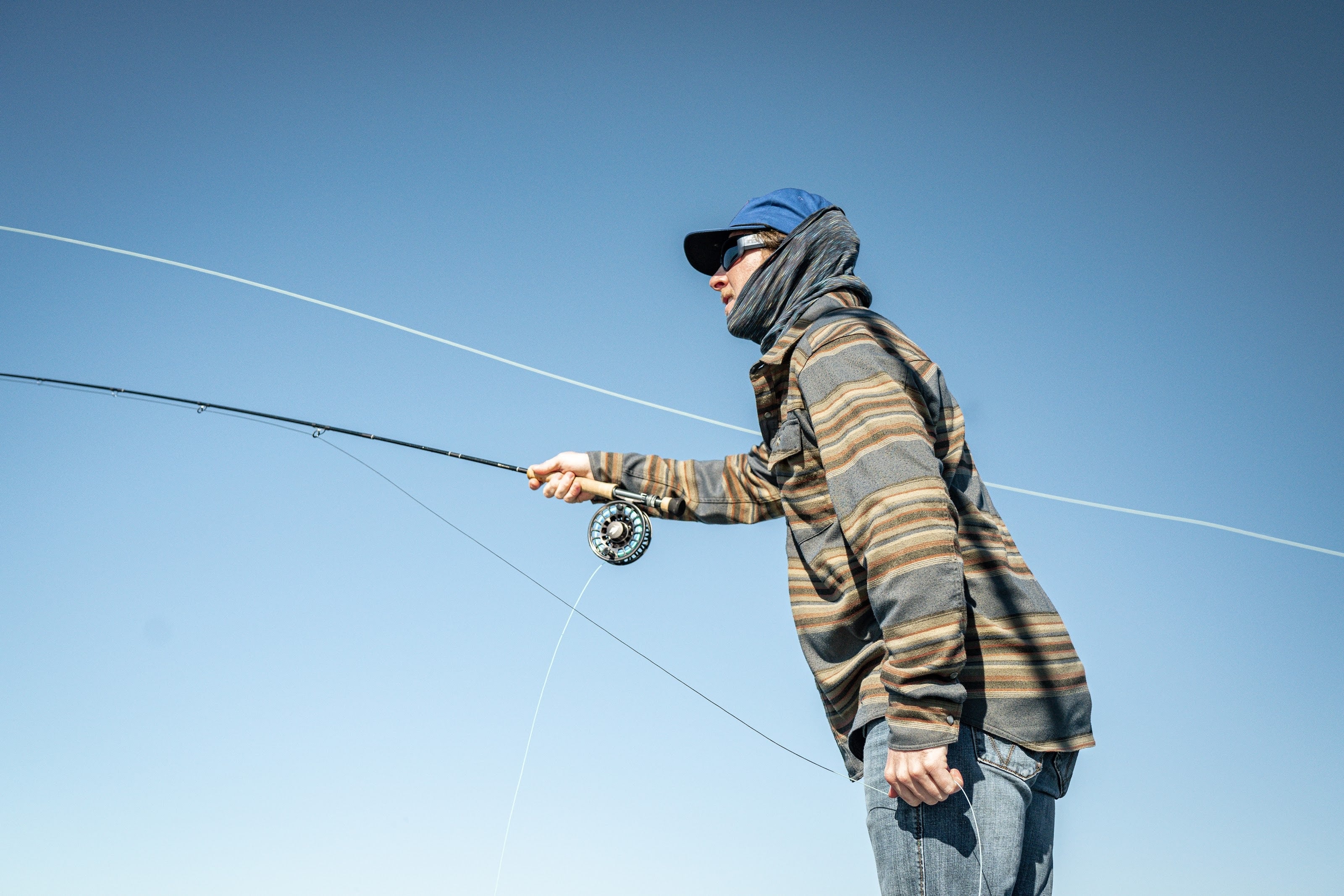 An angler finishing a long fly cast against the sky