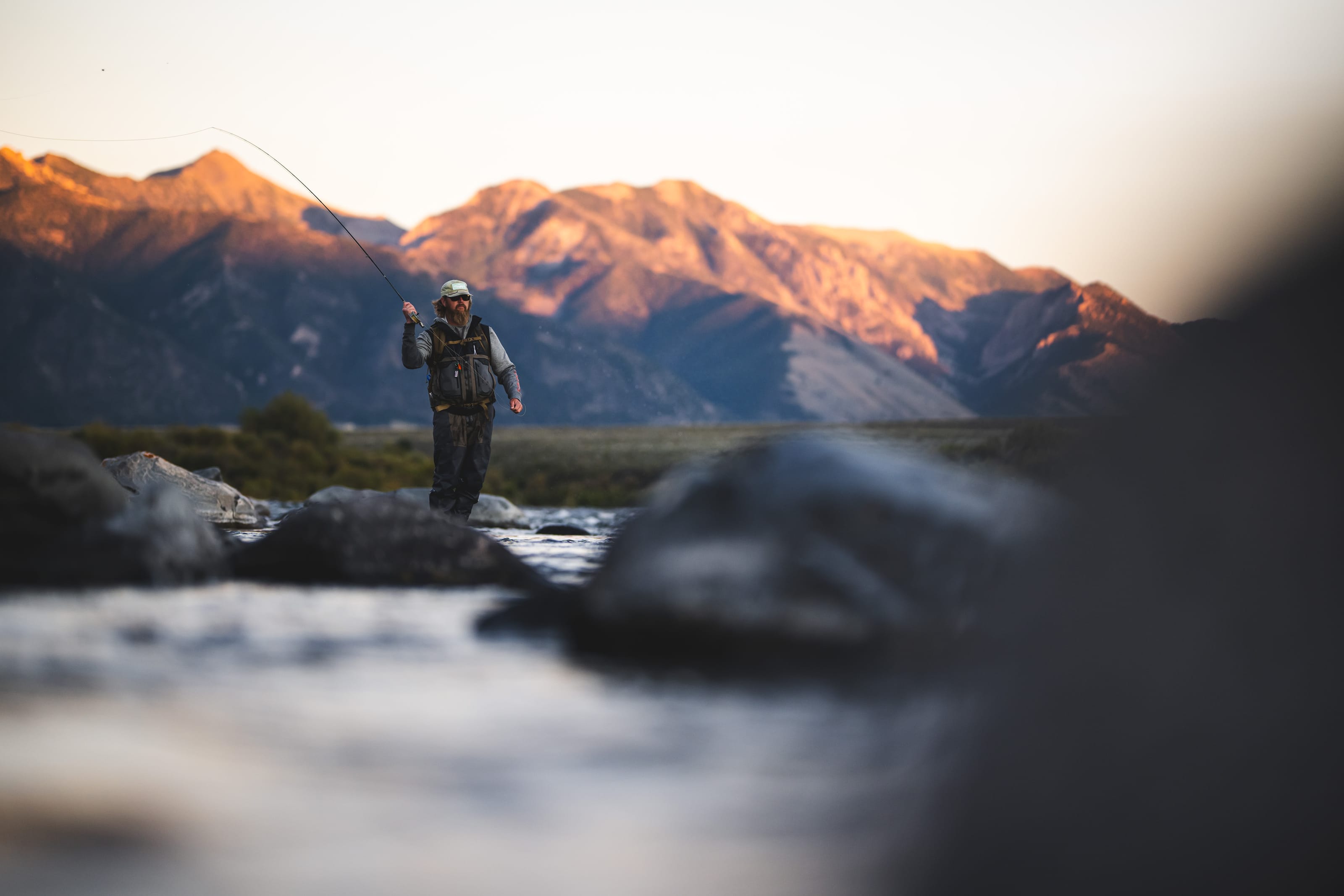 An angler fly fishing a Montana river below mountains lit by low sun