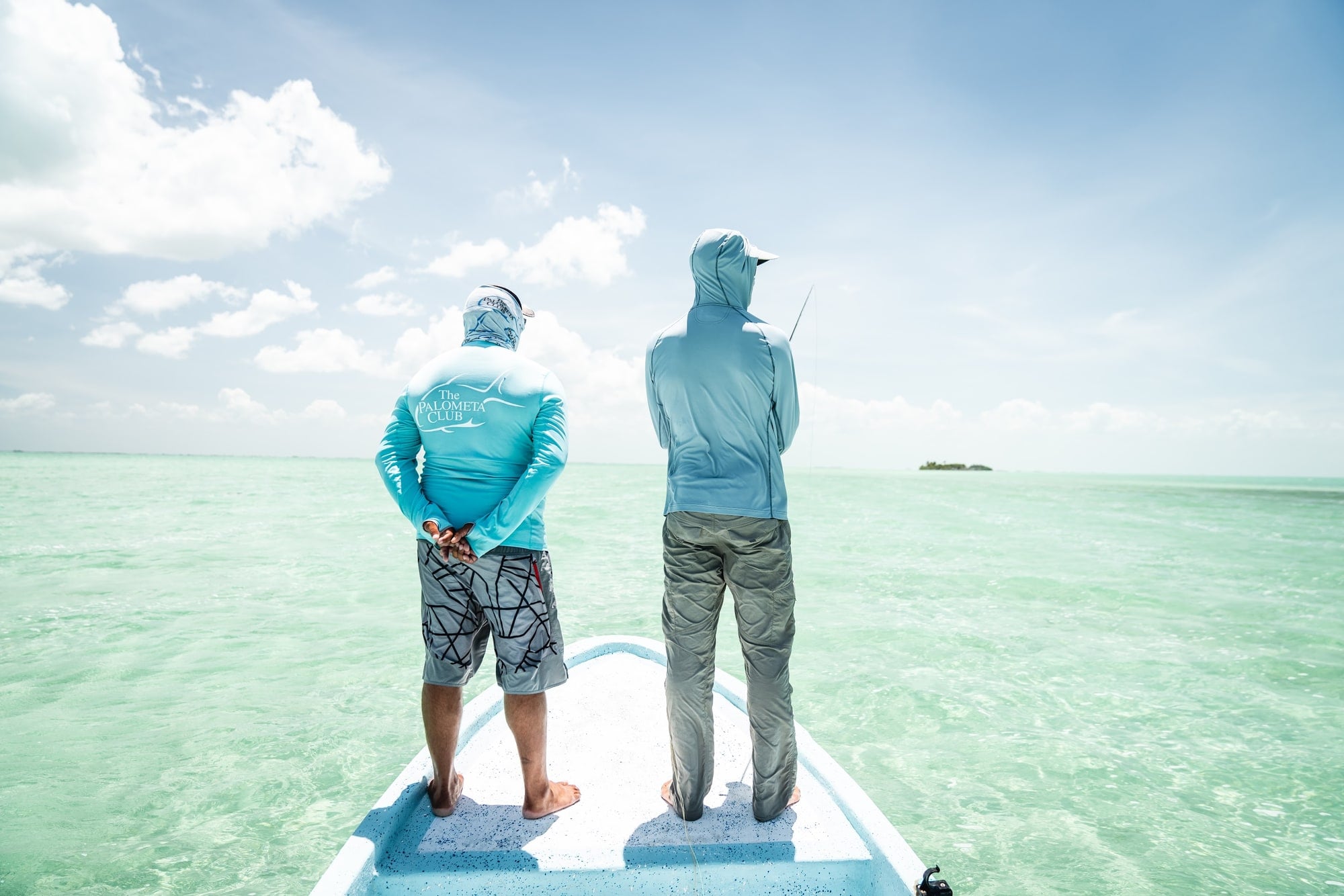 Two anglers on the bow of a skiff looking out over a turquoise flat